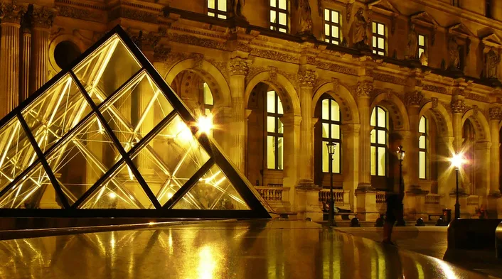 La pyramide du Louvre illuminée de nuit, reflets dorés sur le parvis — Paris