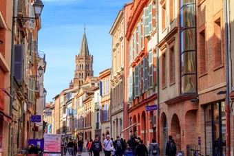 Rue commerçante animée du centre de Toulouse, avec le clocher de la basilique Saint-Sernin en arrière-plan